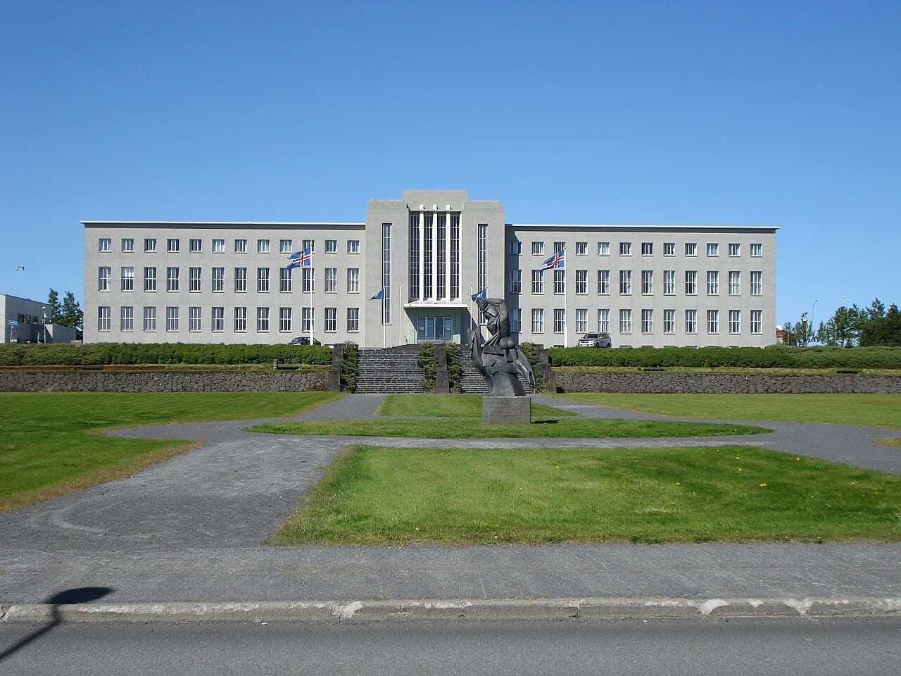 The University of Iceland main building in Reykjavík on a sunny day, with Icelandic flags at the entrance